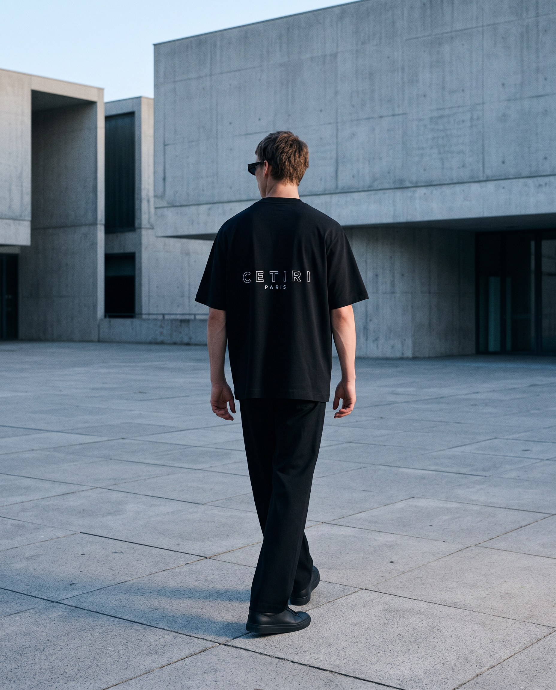 Male model wearing the black CETIRI T-shirt in a concrete architectural setting